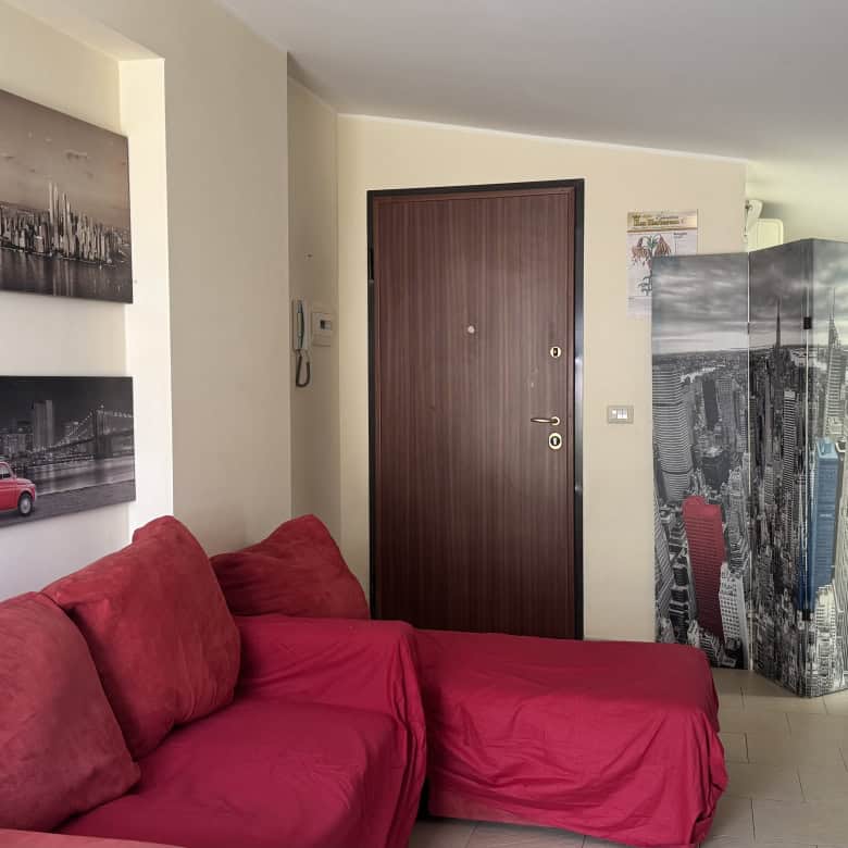 Interno di un appartamento in affitto a Milazzo, con divano rosso e pareti decorate con foto di città.