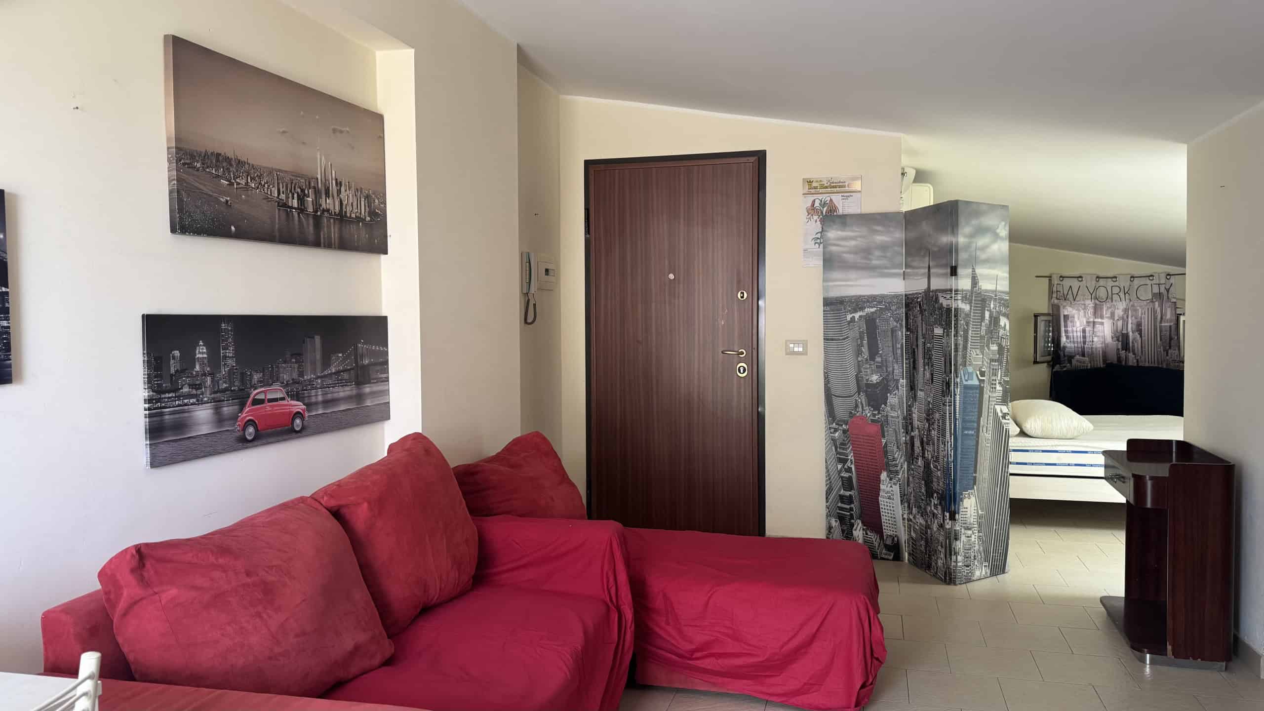 Interno di un appartamento in affitto a Milazzo, con divano rosso e pareti decorate con foto di città.