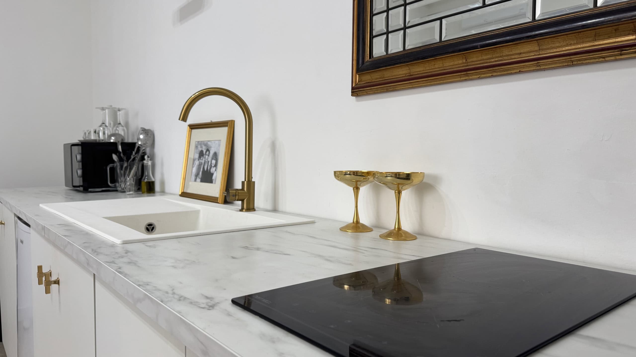 Angolo cucina moderno con piano in marmo, lavello e piano cottura nero, decorato con cornice in legno e accessori in vetro e metallo.