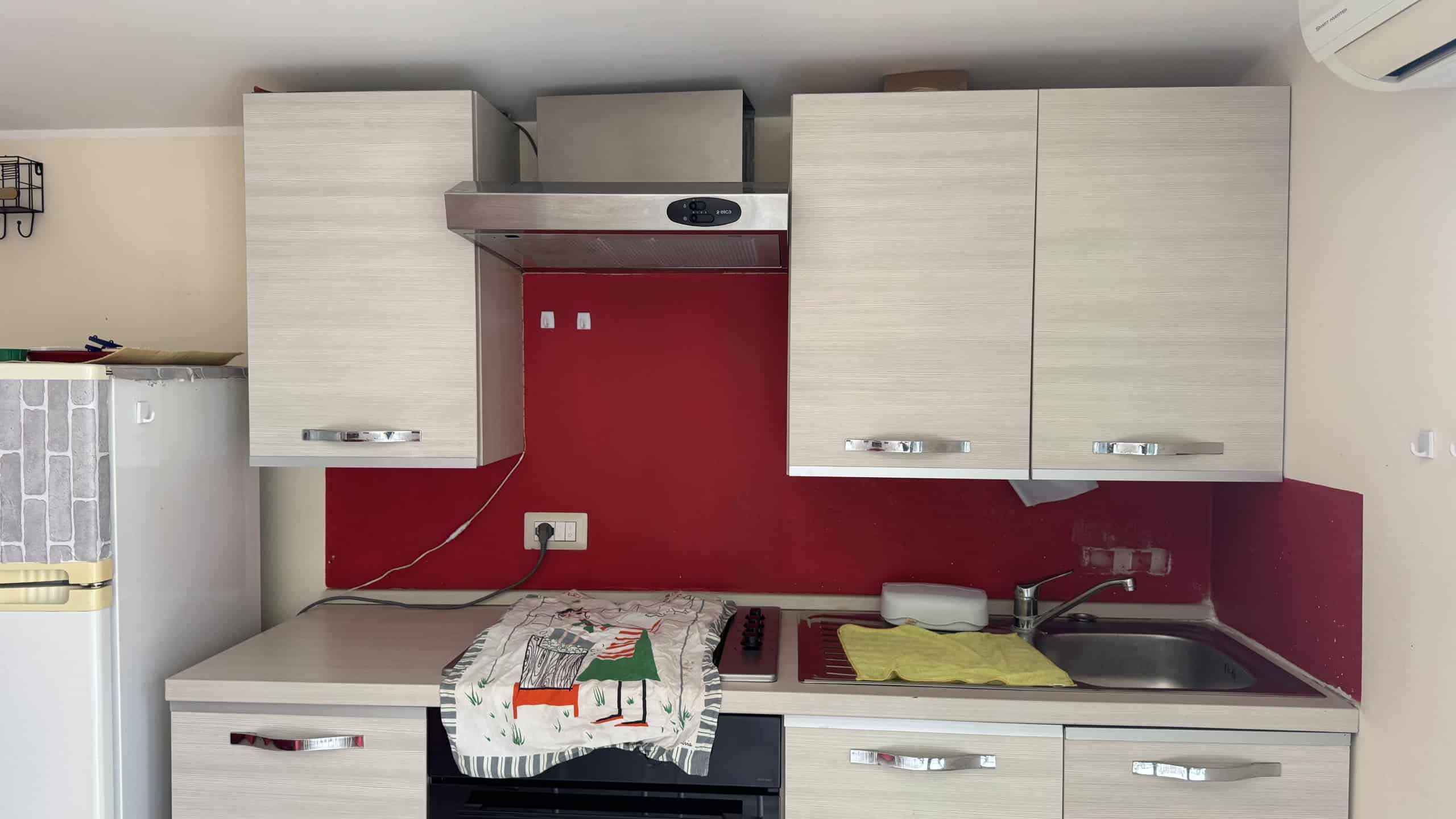 Cucina moderna con ante bianche, piano in acciaio inox e parete rossa, in un appartamento in affitto a Milazzo.