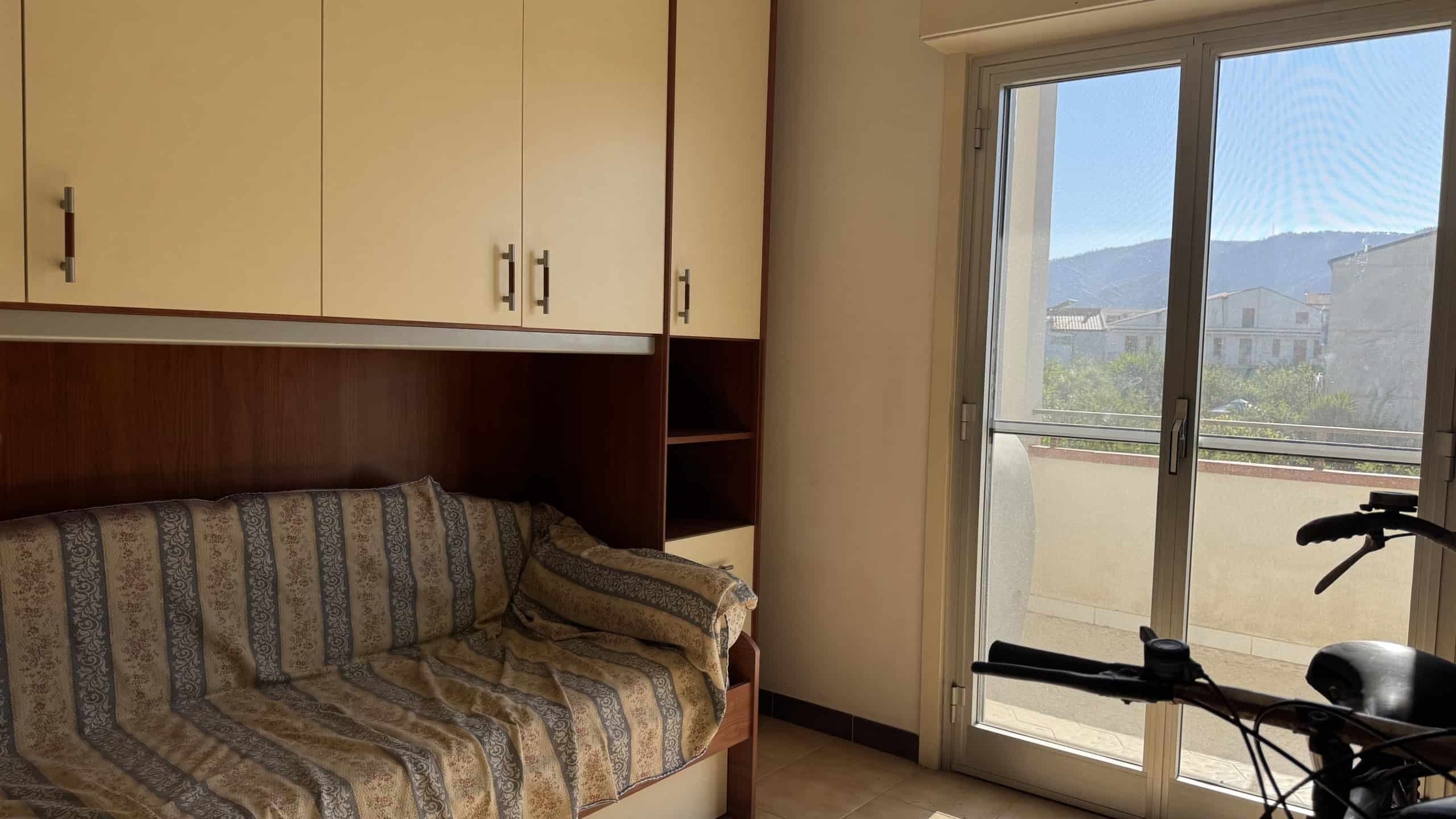 Interno di un appartamento con divano e balcone con vista sulle montagne a Falcone, Me.