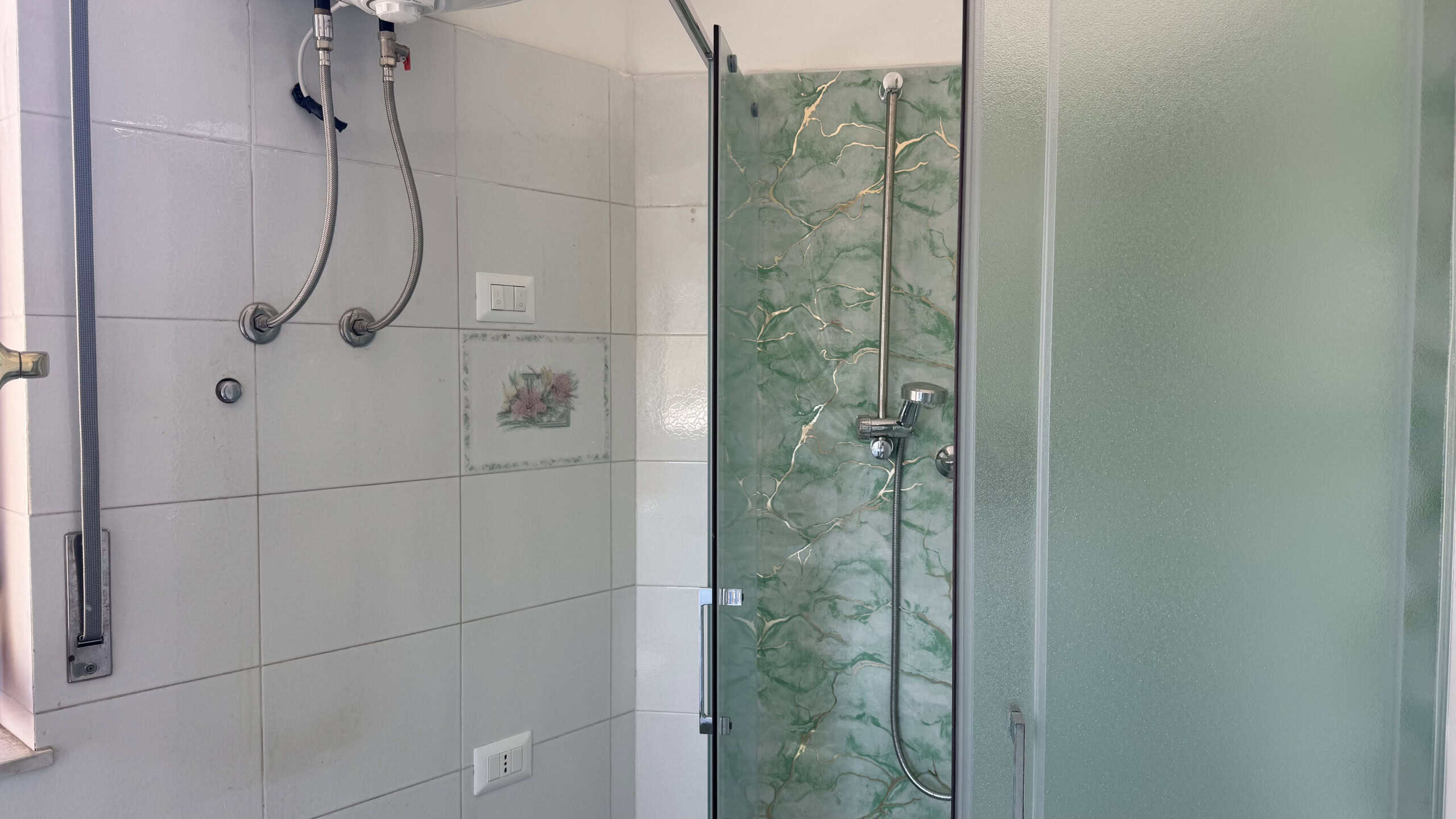 Doccia moderna con parete in vetro e piastrelle verdi, ideale per bagni di case in vendita a Venetico.