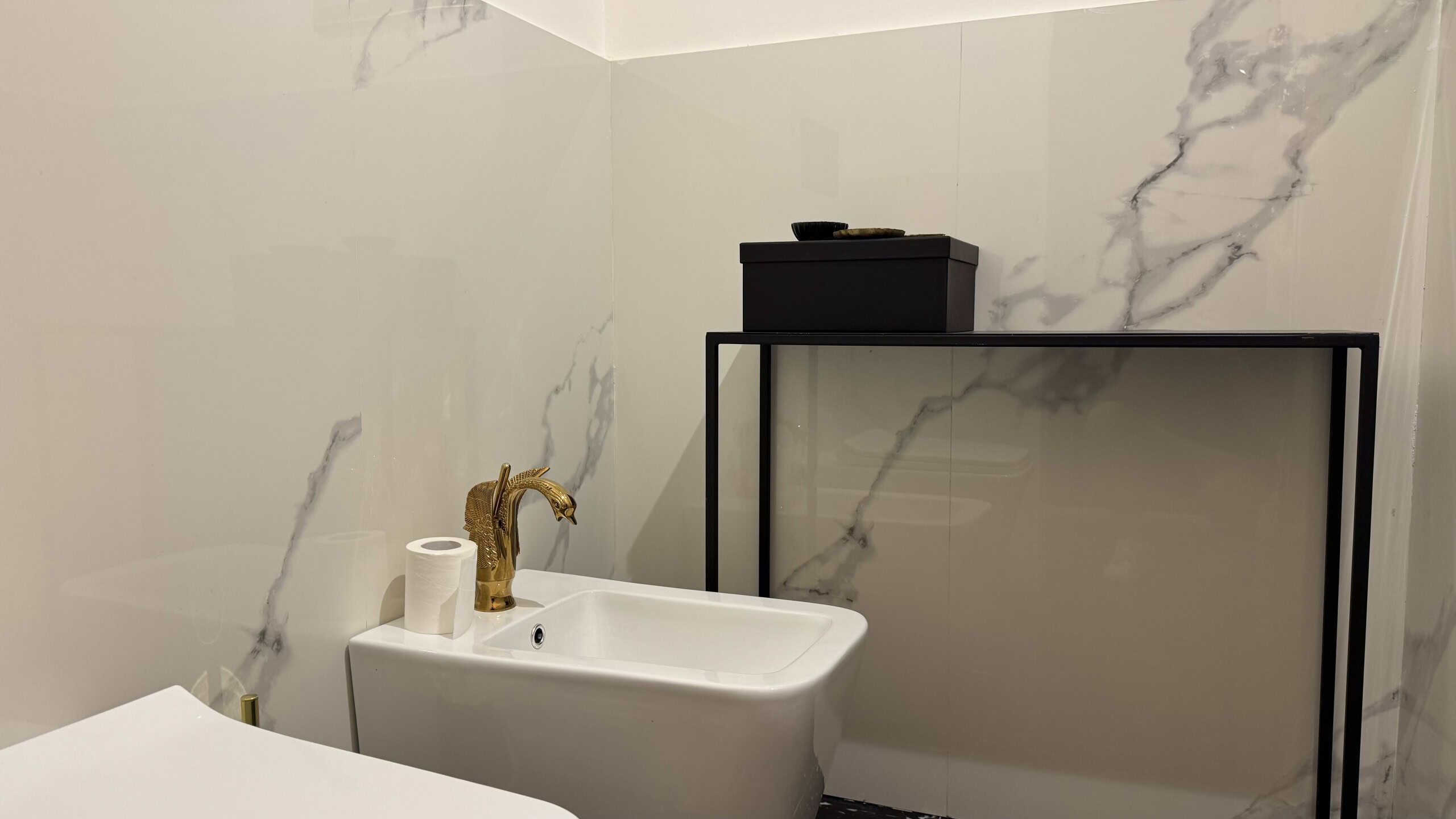 Lavabo moderno in un bagno con pareti in marmo bianco e accessori minimalisti.