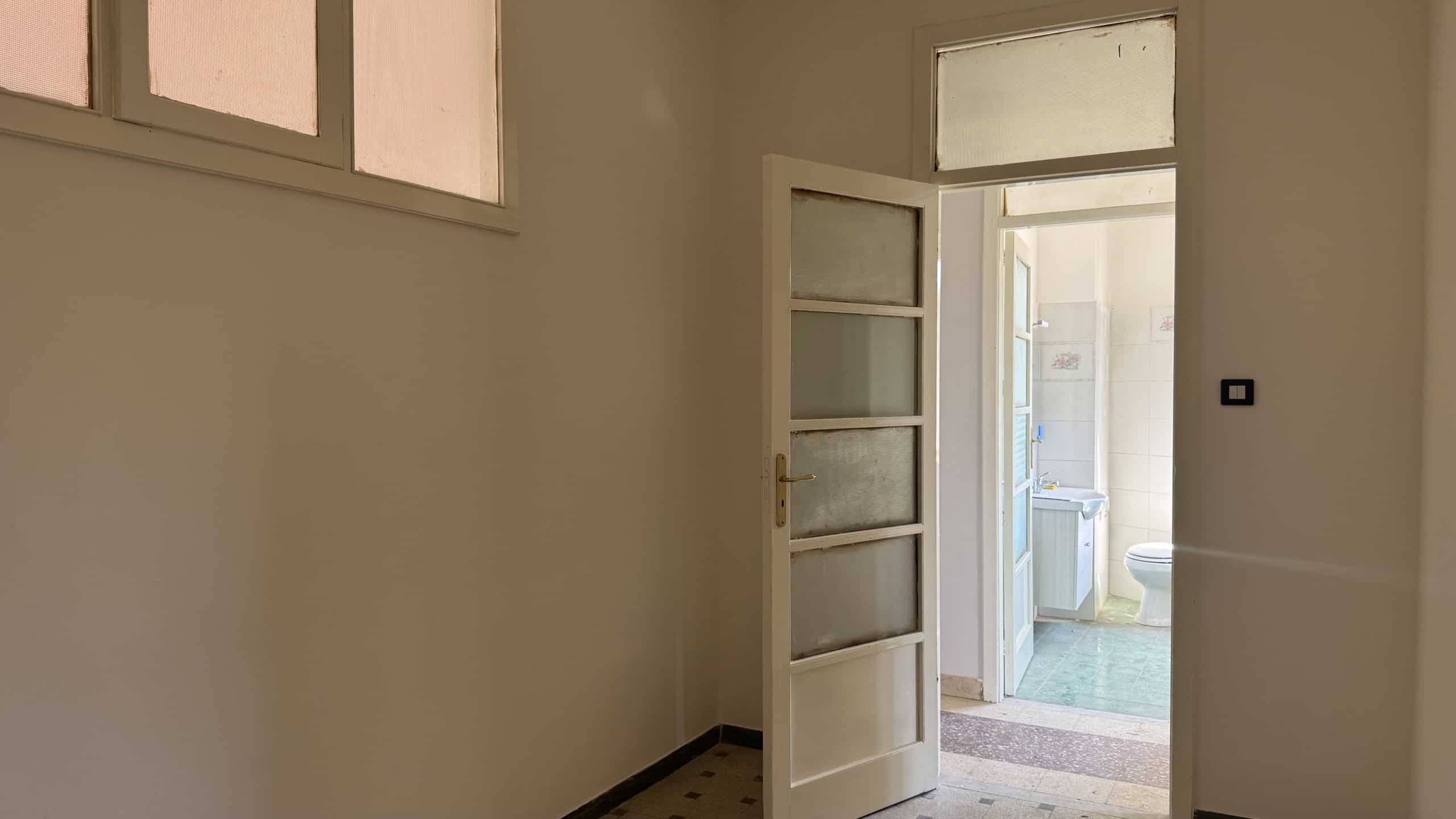 Interno di una casa semindipendente con porta aperta che conduce a un bagno con lavatrice e finestra.