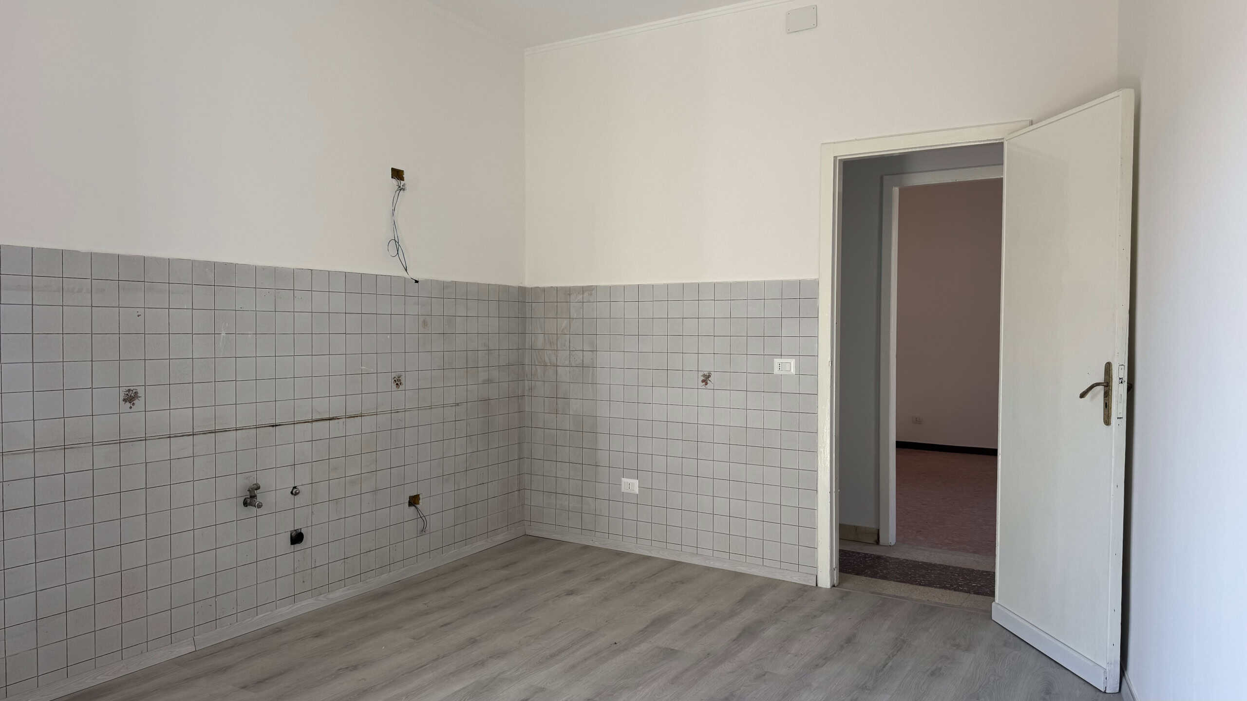 Interno di una cucina in fase di ristrutturazione con pareti rivestite di piastrelle grigie e pavimento in laminato chiaro.
