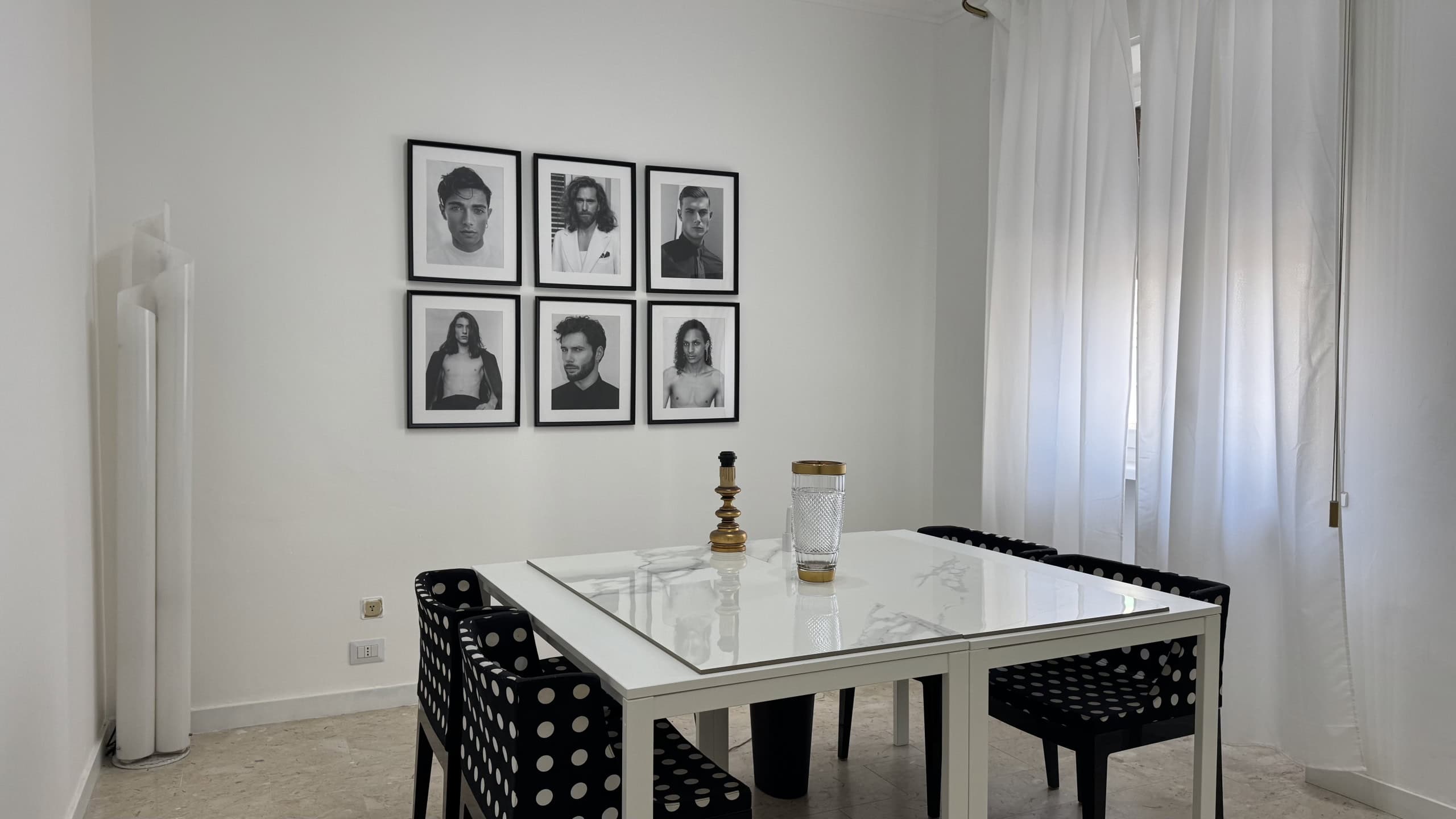 Sala da pranzo moderna con tavolo bianco e sedie nere, decorata con foto in bianco e nero alle pareti e tende bianche leggere.