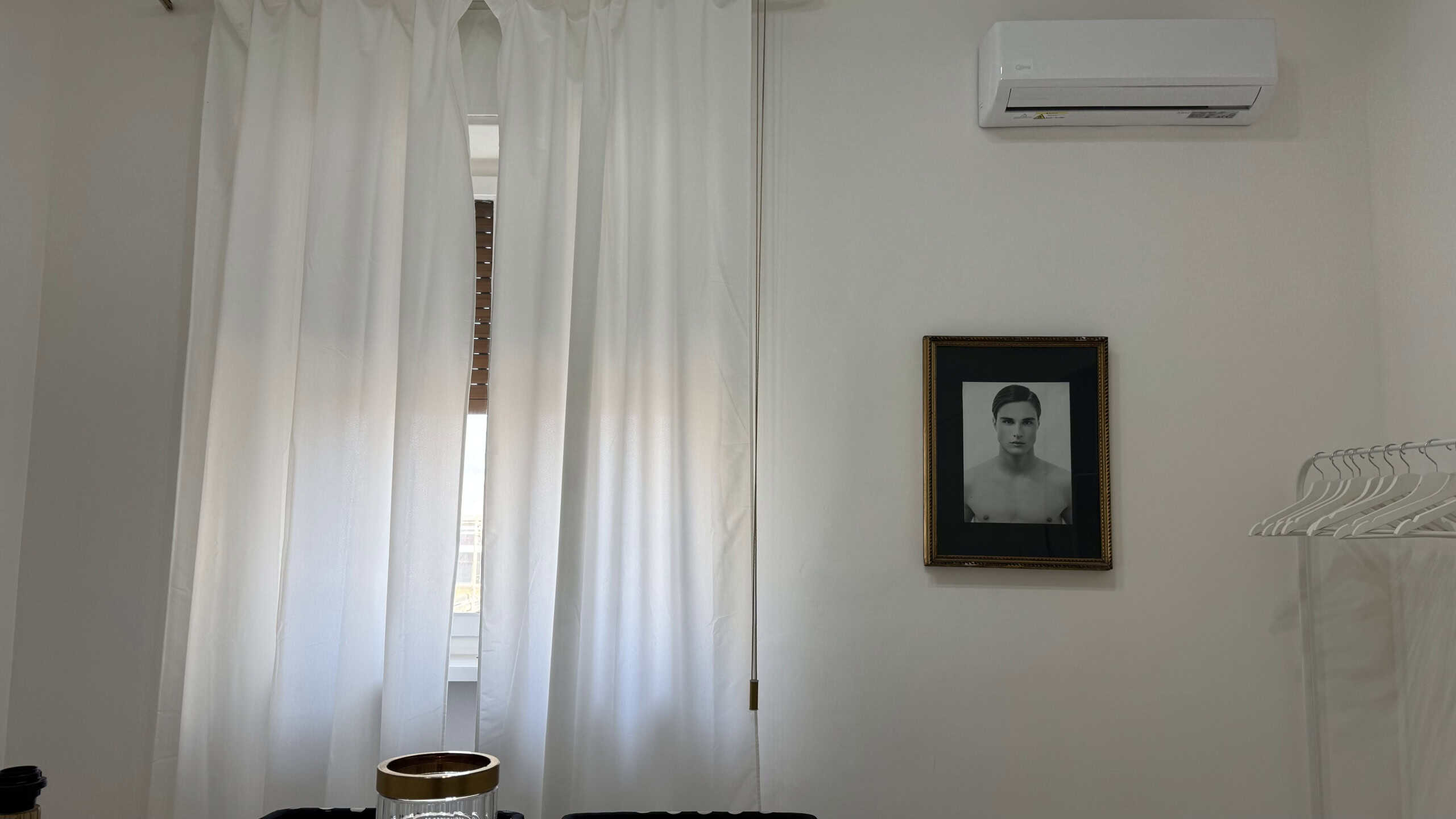 Interno di un appartamento in vendita con pareti bianche, finestra con tende bianche e aria condizionata.