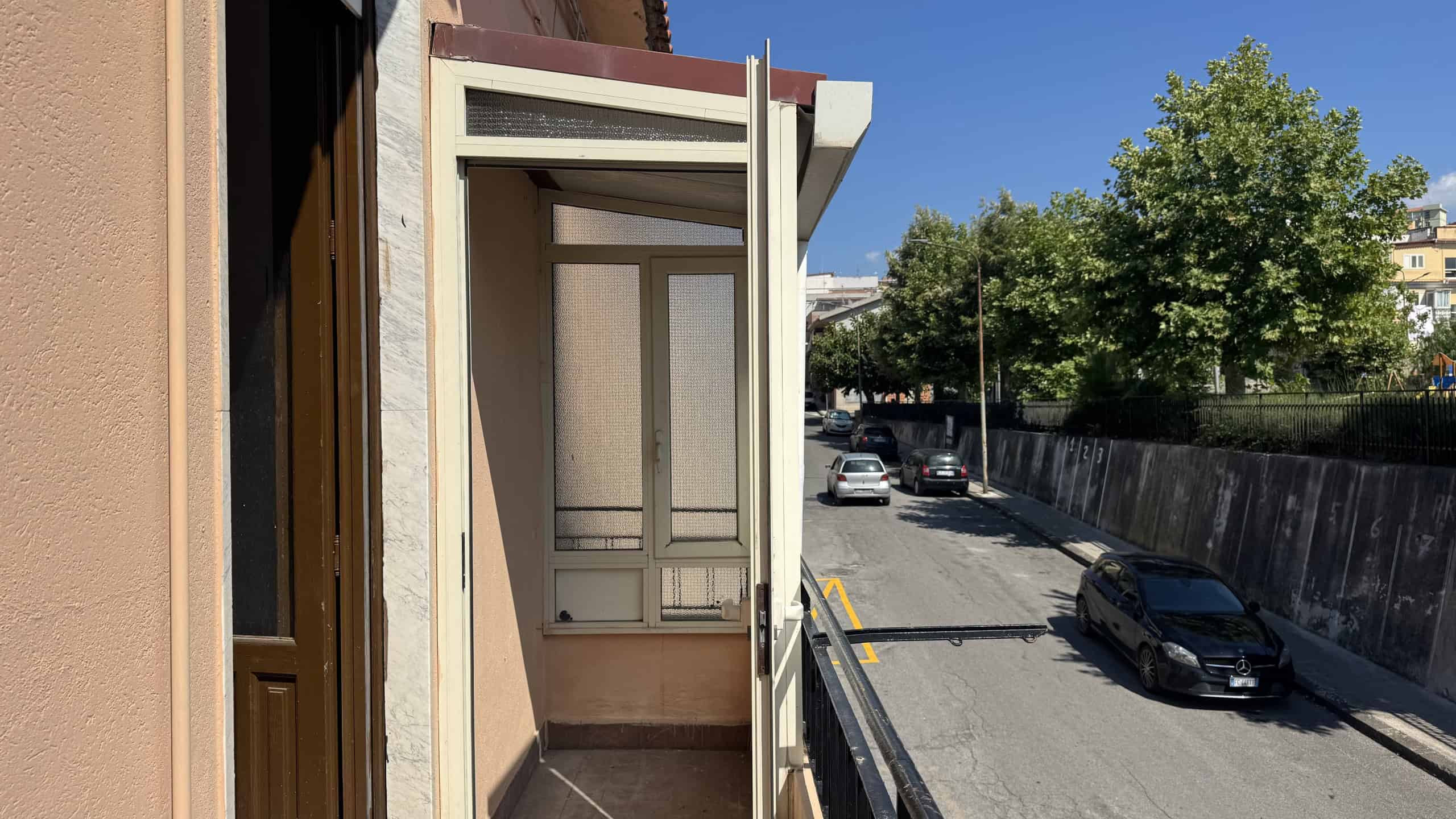 Balcone di una casa in vendita a Venetico con vista sulla strada e su alberi verdi.