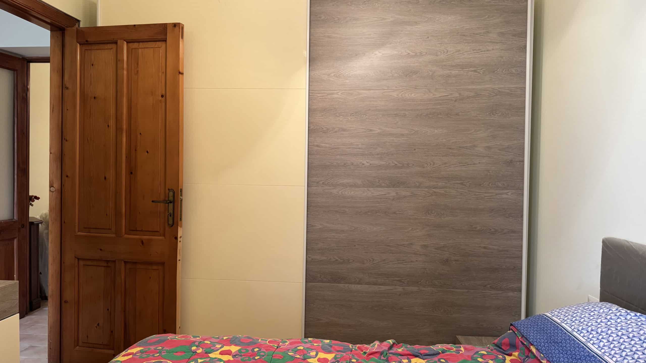 Interno di una camera da letto con parete in legno, porta in legno e letto con copriletto blu e cuscini.