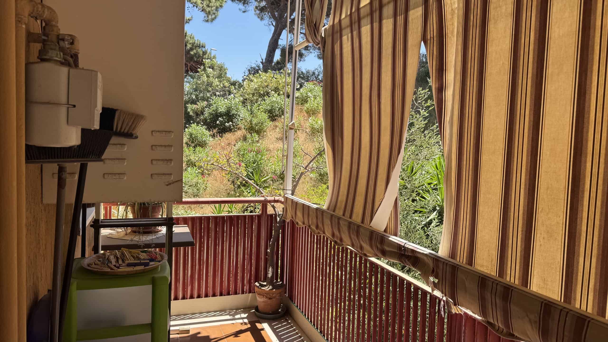 Balcone di un appartamento con vista su natura, tende a strisce e ringhiera in ferro battuto, in zona tranquilla a Messina.
