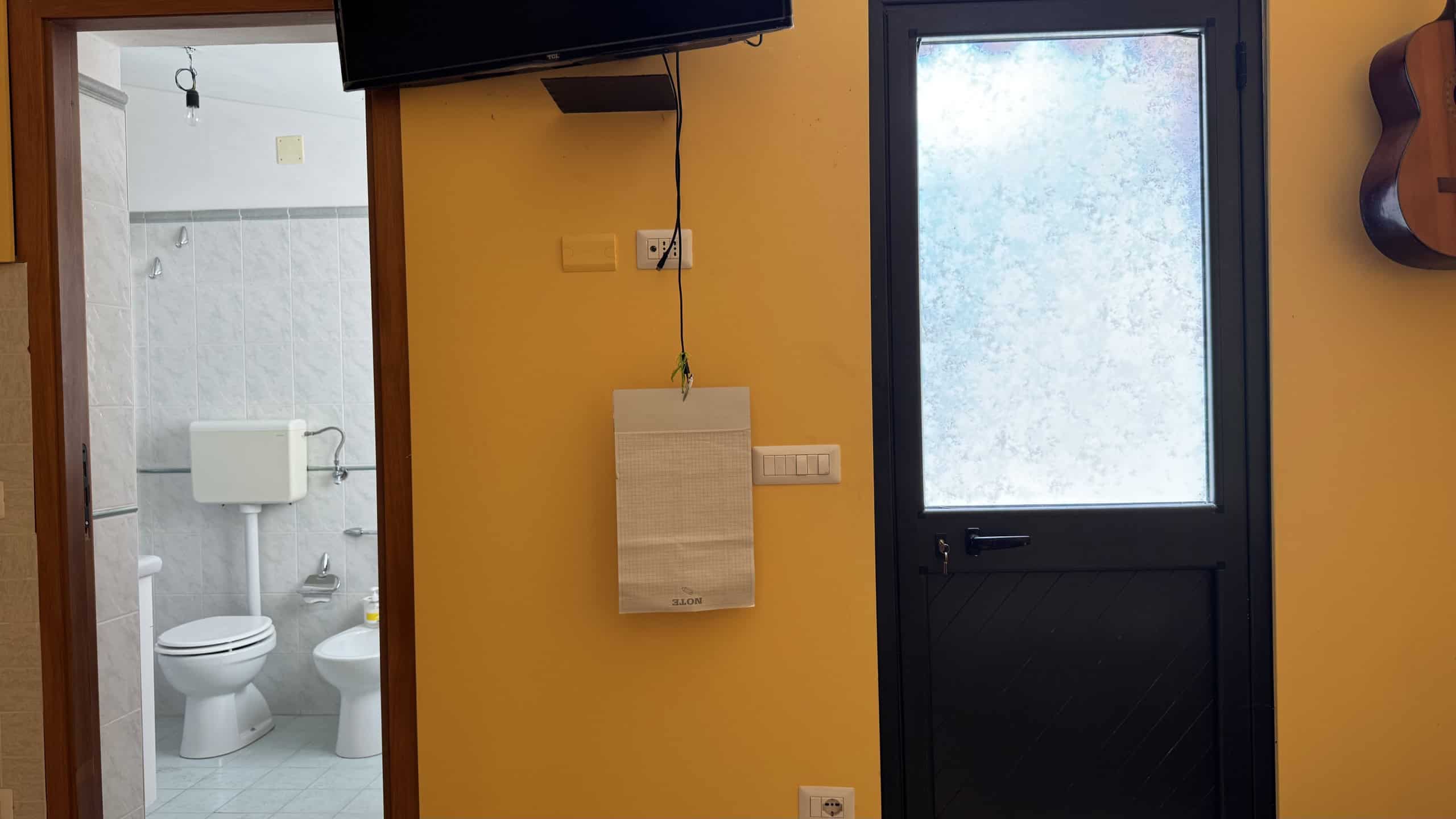 Ingresso di casa indipendente con porta nera e pareti gialle, vista sulla porta e finestra con vetro opaco.
