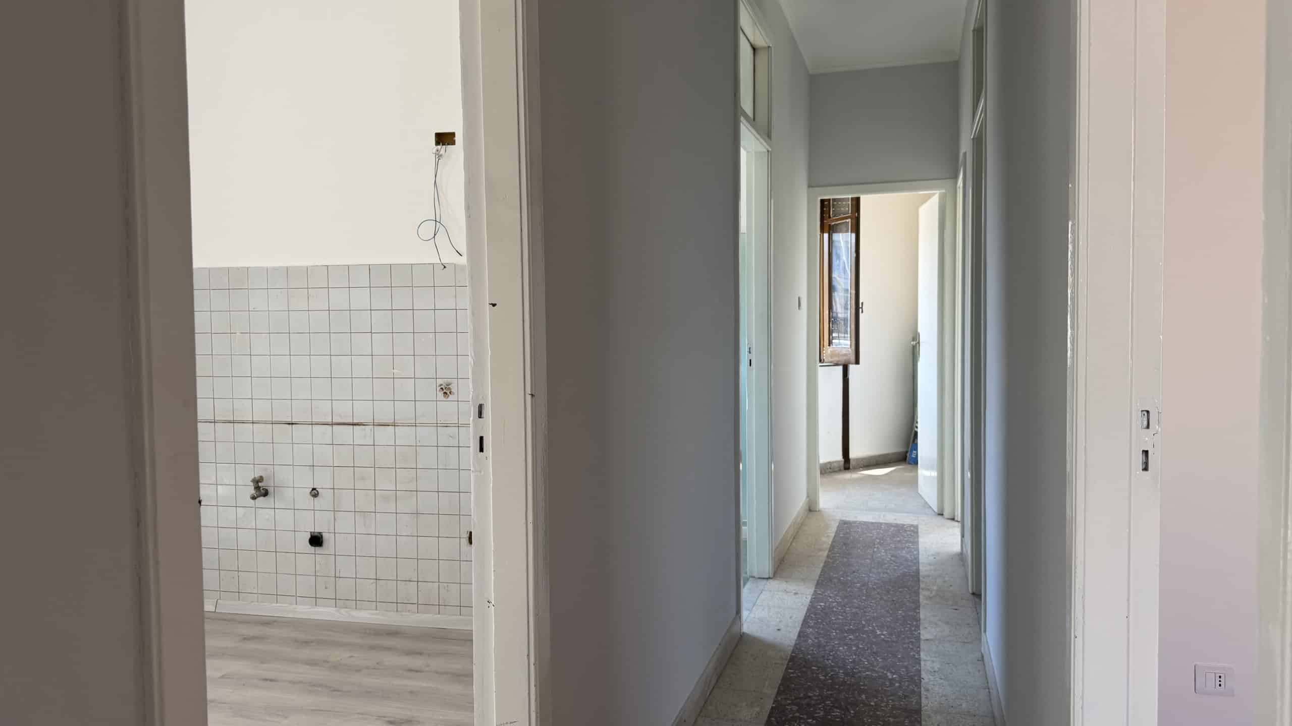 Interno di una casa in vendita a Venetico, vista corridoio con pareti bianche e pavimento in moquette.