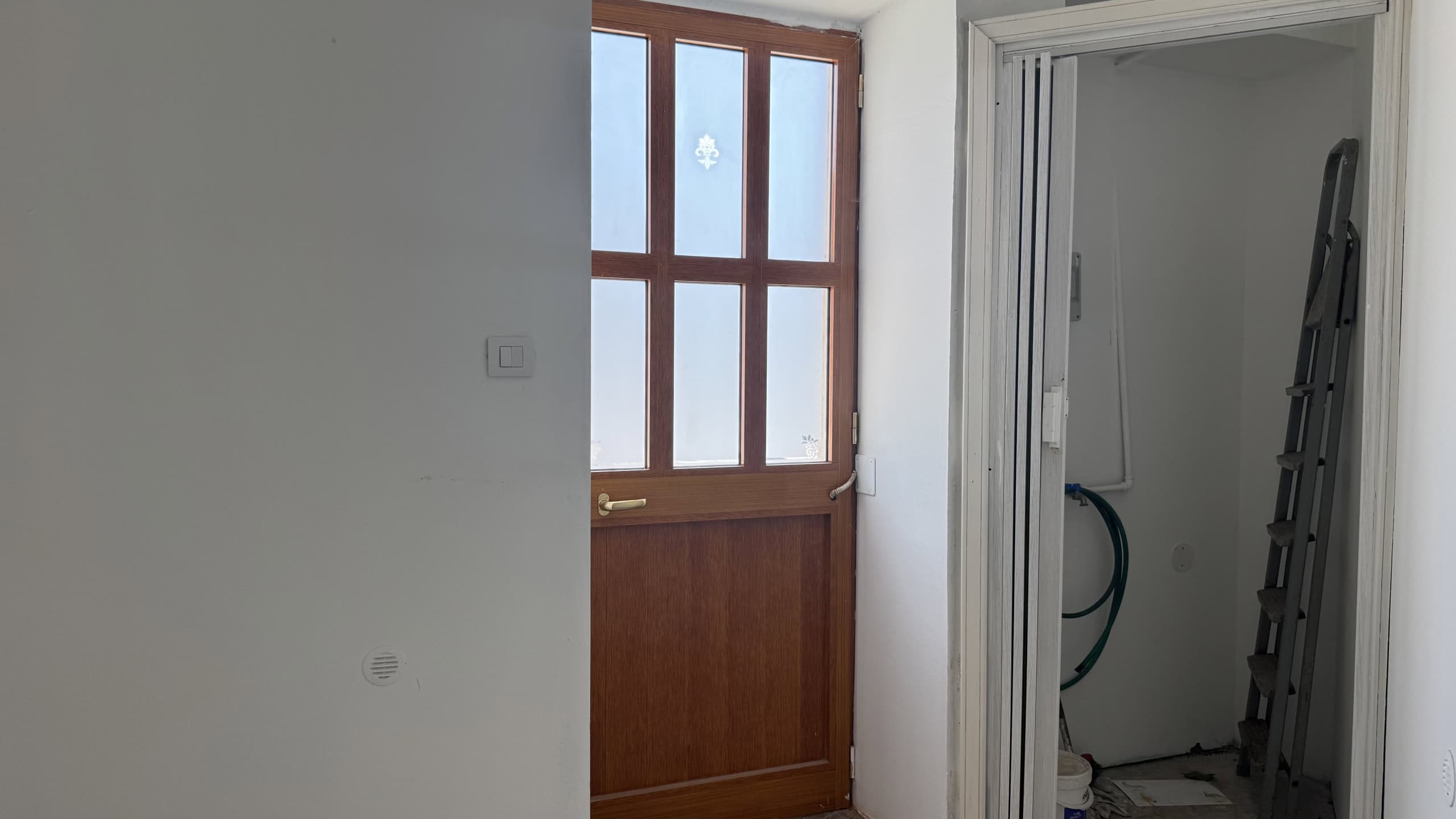 Ingresso di una casa con porta in legno e finestra, vista dall'interno.