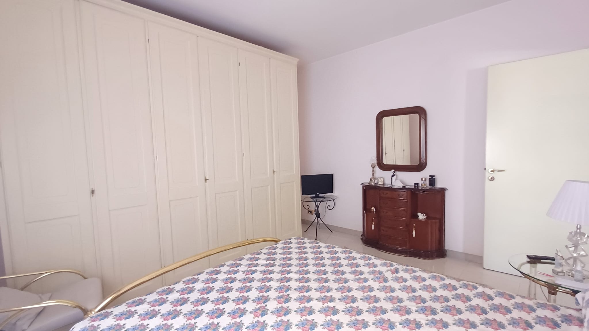 Interno di una camera da letto luminosa con armadio grande, specchio e mobili classici in un appartamento in vendita a Capo d'Orlando.
