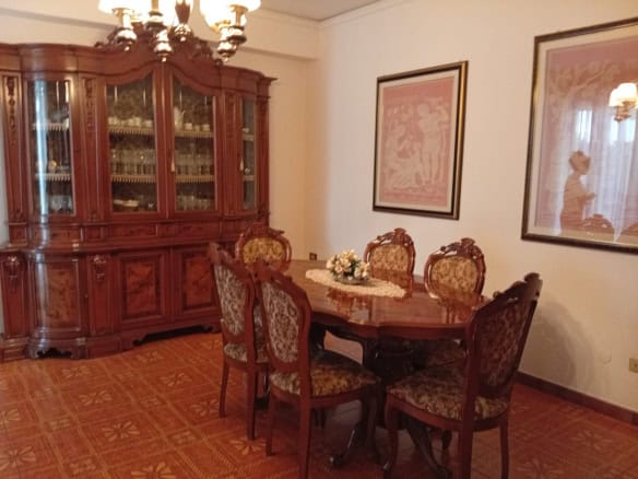 Elegante sala da pranzo con tavolo rotondo e sedie in stile classico, grande credenza in legno e decorazioni artistiche alle pareti.