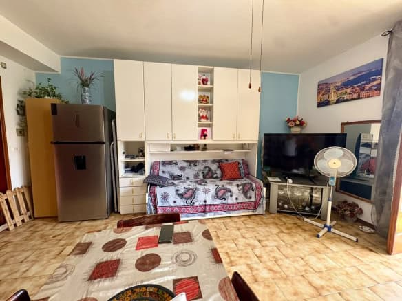 Interno di un monolocale con cucina, divano e TV, arredato in stile semplice e funzionale.