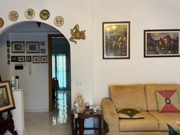 Interno di un soggiorno con pareti decorate con quadri e piatti, divano beige con cuscini, e arredi classici in stile tradizionale.