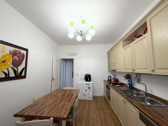 Cucina moderna con mobili beige, tavolo in legno e illuminazione a soffitto con lampadario a globi.